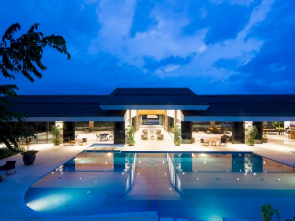 Modern hotel courtyard with a lit swimming pool and lounge terrace under a vivid blue dusk sky.