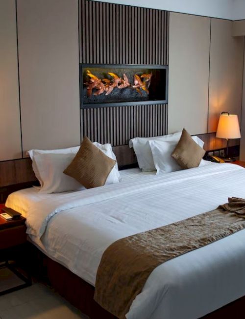 A modern hotel room with a made bed, bedside lamps, and a lit fireplace feature in the wall.