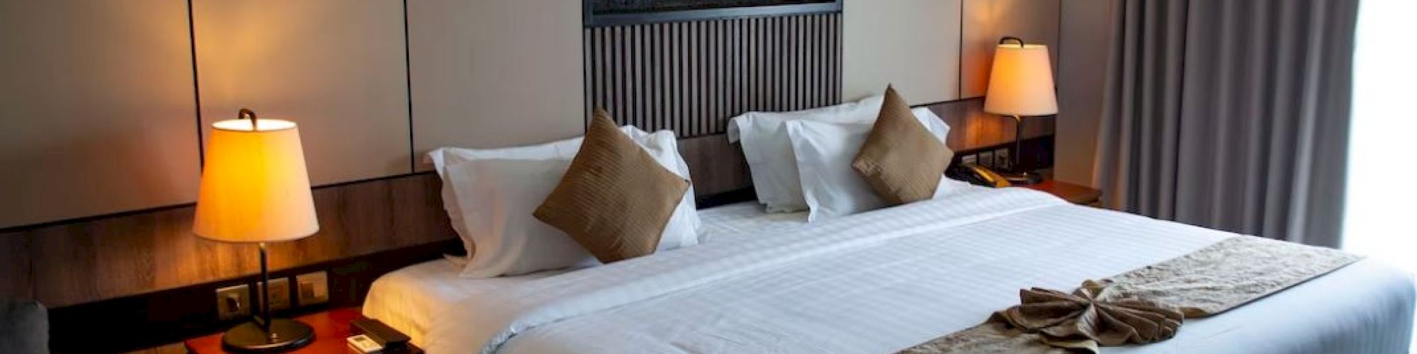 A modern hotel room with a neatly made bed, bedside lamps, and a wall fireplace glowing behind the headboard.