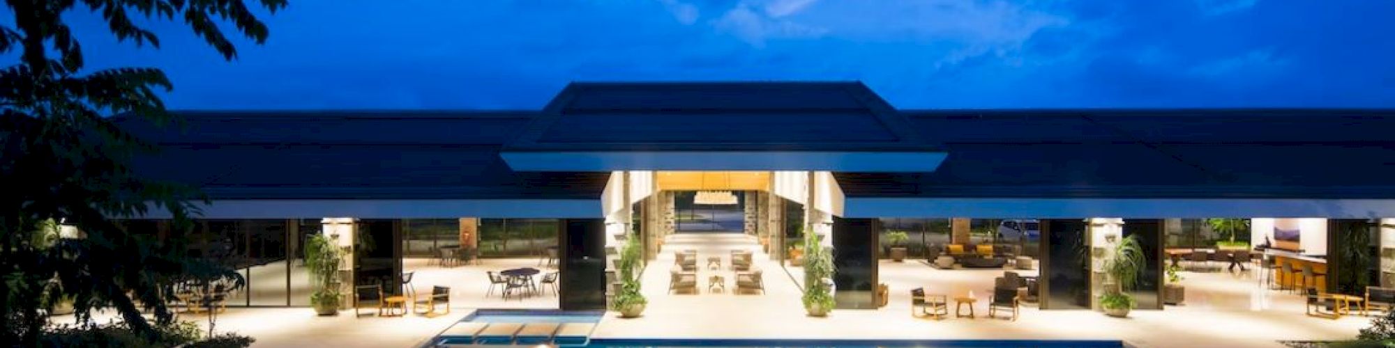 A blue-hour resort scene shows an outdoor swimming pool with lounge seating and a bright sky behind.