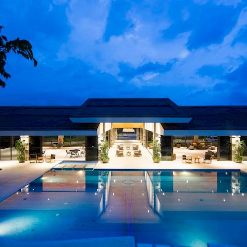 A sleek outdoor hotel pool at dusk, framed by lounge chairs and a modern pavilion under a deep blue sky.