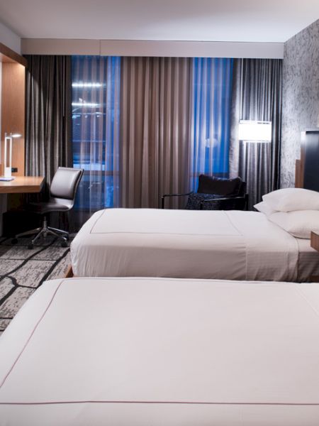 A modern hotel room with two neatly made beds, wood paneling, curtains, and bedside lamps.