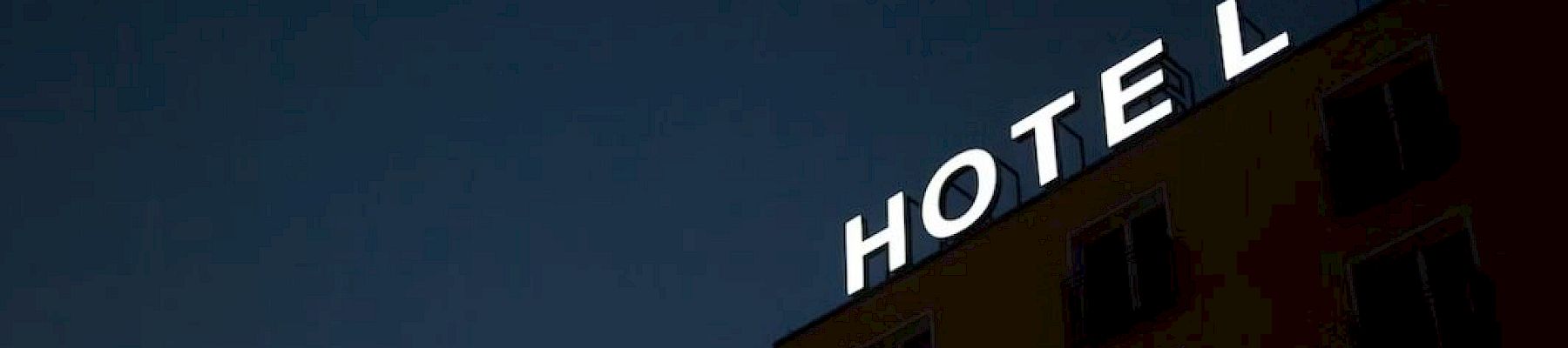 A building at night with a bright HOTEL sign across its top under a dark blue sky.