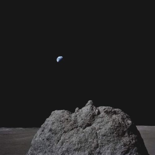 A small blue planet floats above a rough gray rock against a dark, minimal background.