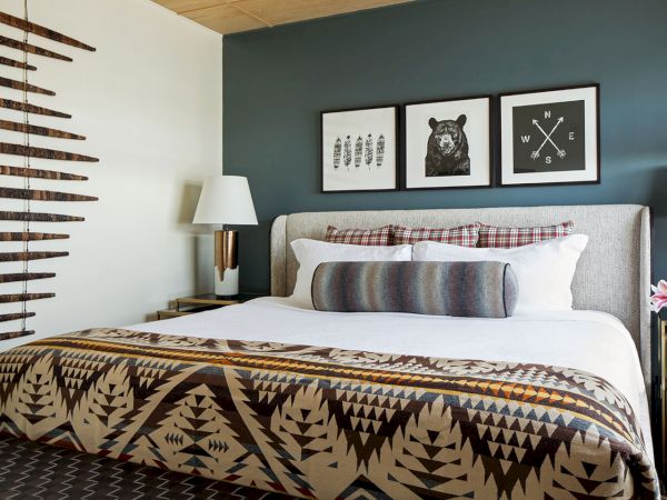 A cozy modern bedroom with a lit bedside lamp, patterned blanket, and three framed prints above the bed.