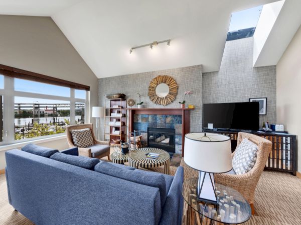 A modern living room with a fireplace, TV, cozy seating, and large windows overlooking a waterfront view.