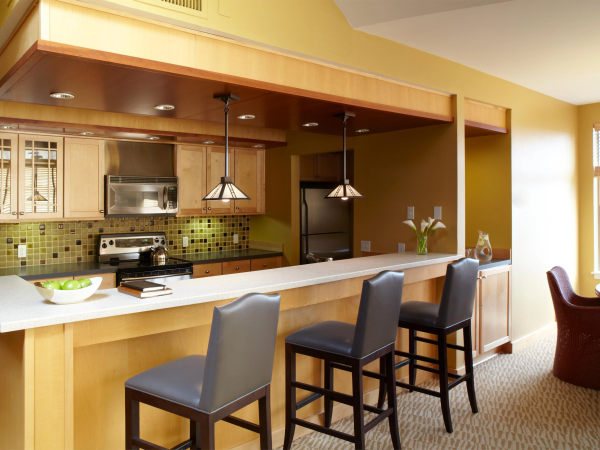 A modern home kitchen with a central island, pendant lights, stove, microwave, and bar stools, all under warm lighting.