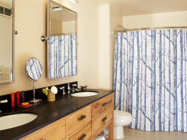 A modern bathroom with a dark vanity sink, flower, mirror, and a blue-and-white forest-pattern shower curtain.
