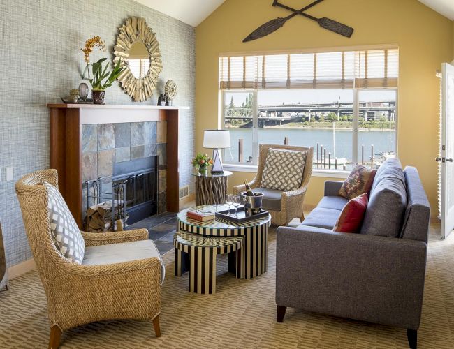 Cozy living room with a fireplace, upholstered seating, and a large window overlooking a river and bridge.