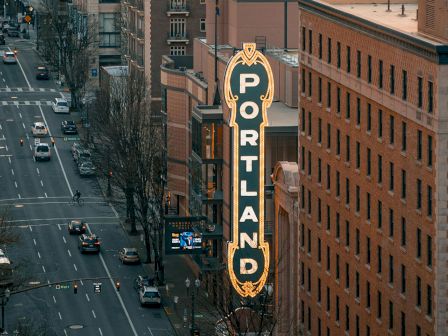 Busy downtown street view with a glowing vertical sign reading PORTLAND.