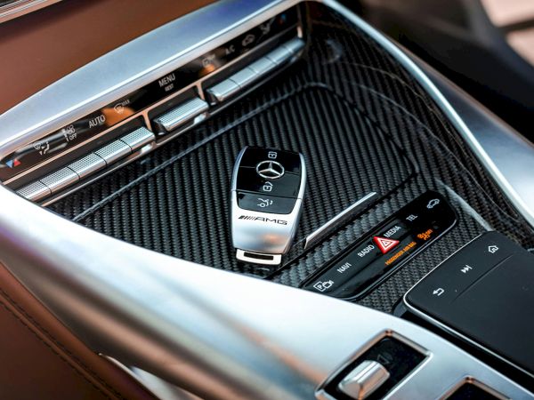 A Mercedes-AMG car console with carbon-fiber trim and illuminated steering/control buttons, including an AMG badge and media controls.