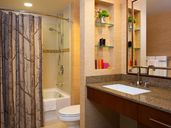 Modern bathroom with a glass shower, bathtub, granite vanity, mirror, and wall shelves with toiletries and decor.