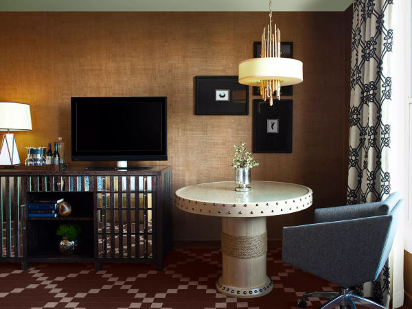 A modern lounge: round table with lamp and flowers, framed art on the wall, TV/media console, and patterned curtains.