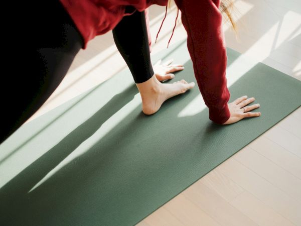 People practice yoga on green mats, holding a plank-like pose with hands on the floor and legs extended.