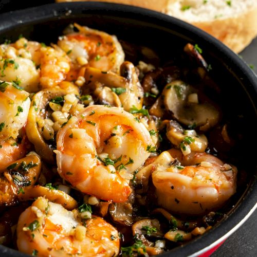 A skillet of saut&eacute;ed shrimp with mushrooms and garlic, coated in a savory sauce and topped with chopped parsley.