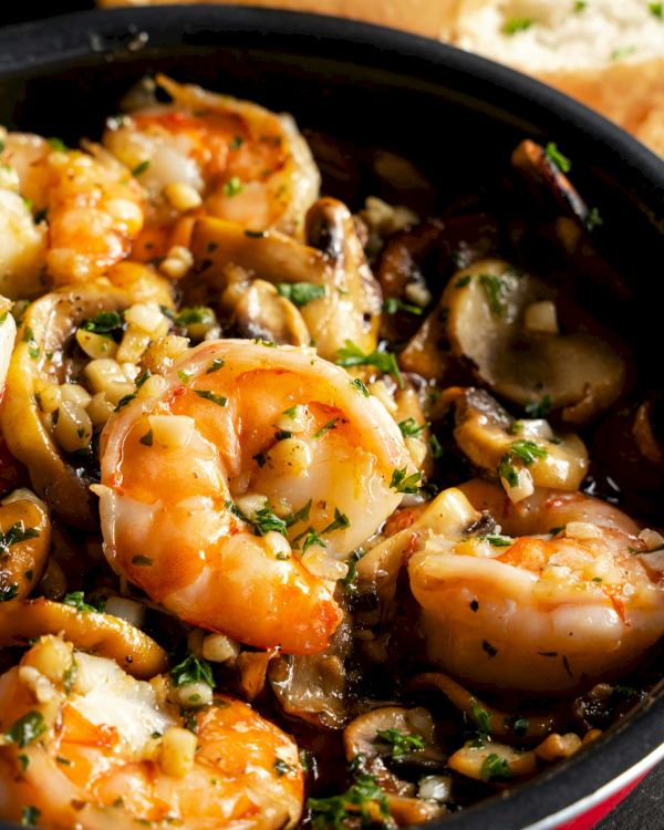 A skillet of saut&eacute;ed shrimp with mushrooms and garlic, coated in a savory sauce and topped with chopped parsley.