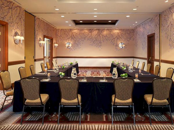 A formal meeting room with a long set dining table, chairs, flowers, and warm lighting.