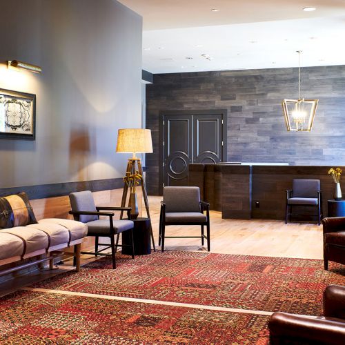A modern reception lounge with upholstered chairs, sofa, patterned rug, wall art, and pendant lamps.