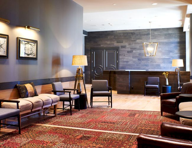 A modern reception lounge with upholstered chairs, sofa, patterned rug, wall art, and pendant lamps.