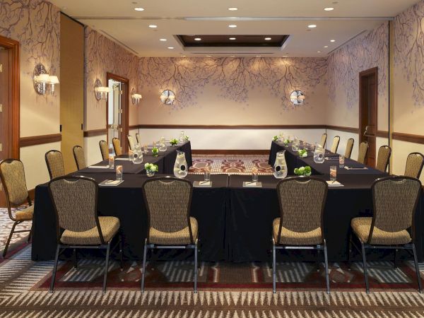 A formal meeting room with a long banquet table set for dining, chairs, decorative flowers, and wall sconces with patterned wallpaper.