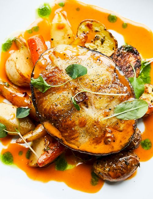 Roasted chicken with herb garnish and root vegetables served over orange sauce in a white bowl.