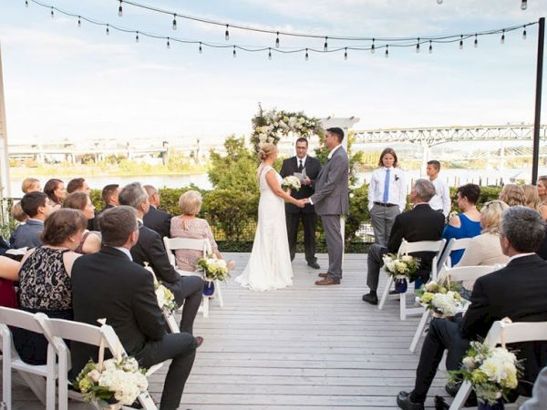 An outdoor wedding ceremony on a deck with the bride and groom at the aisle, while guests sit on both sides.