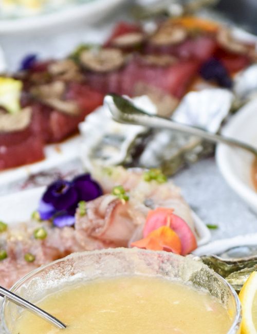 A seafood spread with shrimp, fish, and lemon garnish on a buffet table, served with spoons and side dishes.