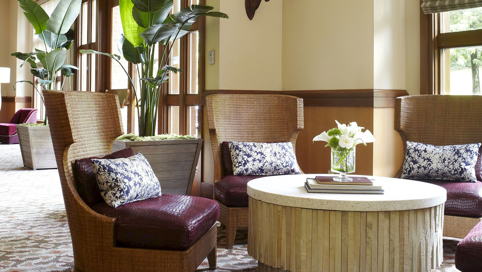 A cozy lounge with wicker chairs, patterned pillows, and a round coffee table topped with a vase of white flowers.