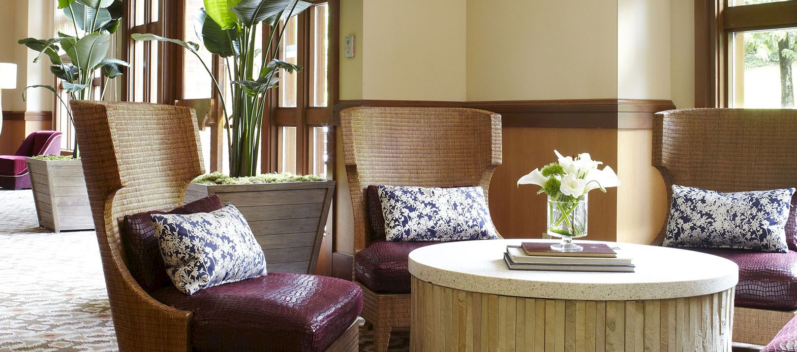 A cozy lounge with wicker chairs, patterned pillows, and a round coffee table topped with a vase of white flowers.