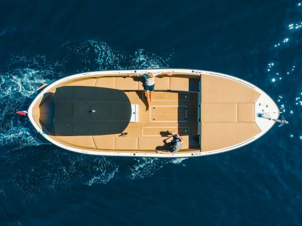 A luxury yacht floats on blue water as people relax on deck, with waves splashing from above.