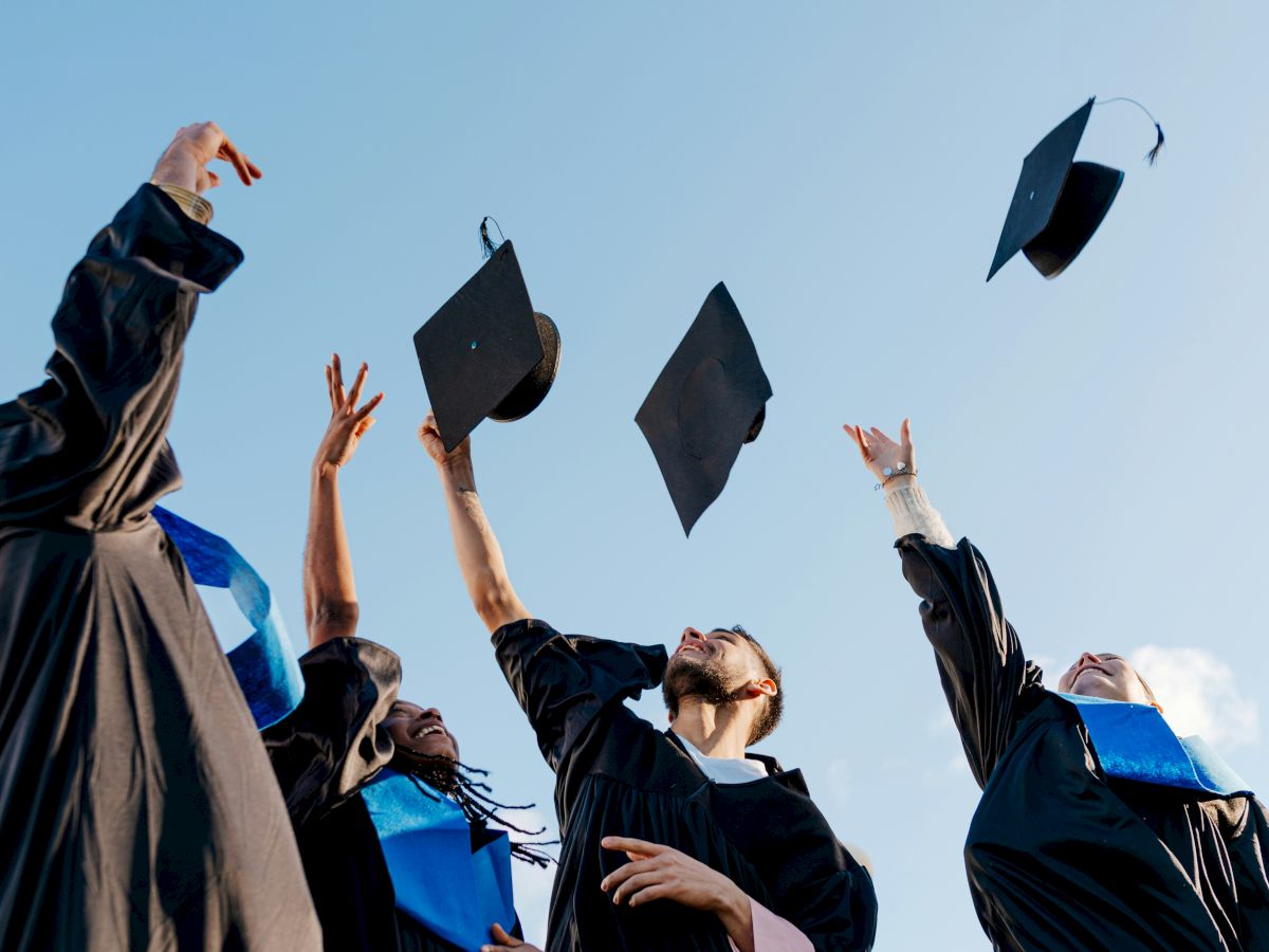 Graduates in caps and gowns toss graduation hats into a clear blue sky, celebrating their achievement and new beginnings.