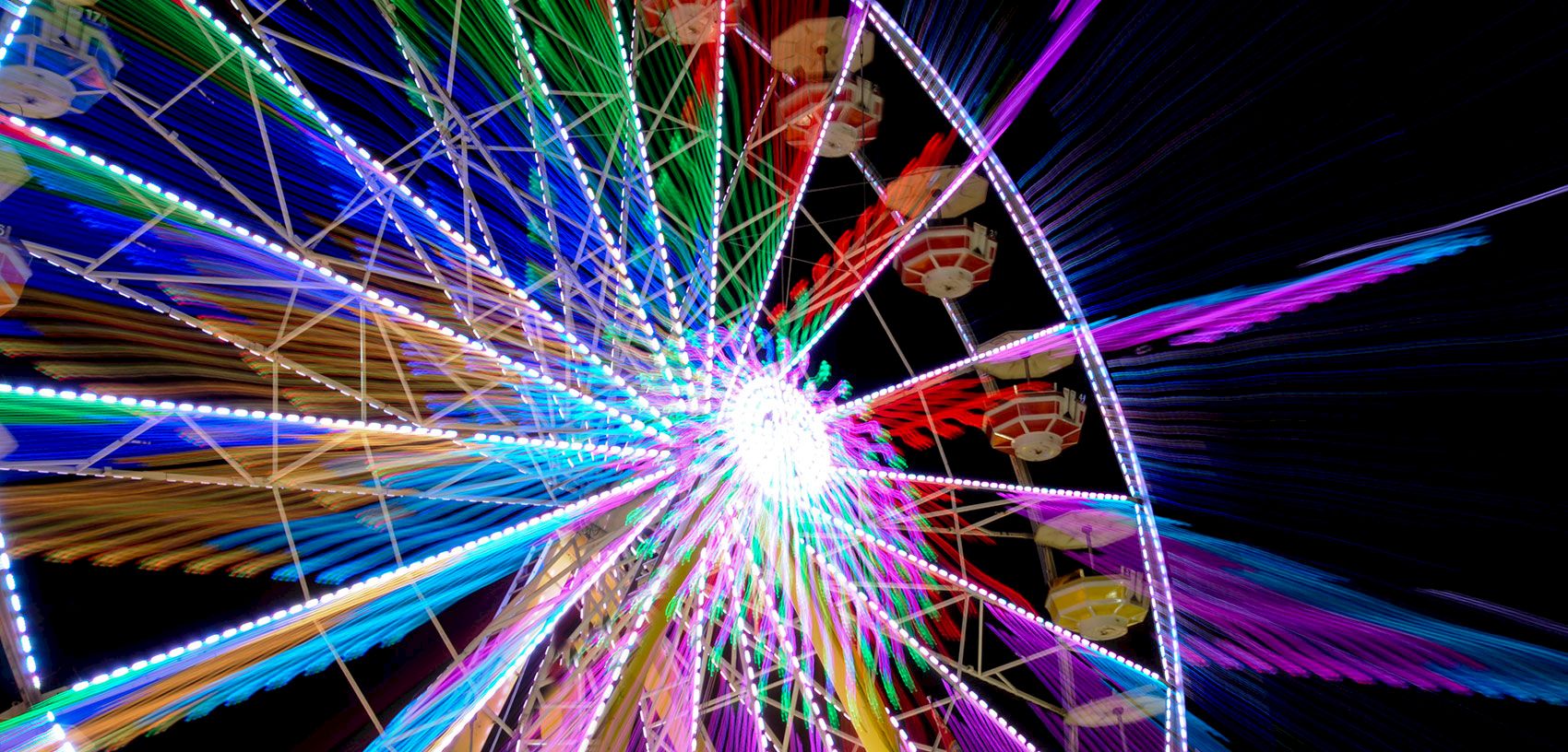 Colorful amusement-park ferris wheel lights streak in motion blur at night.