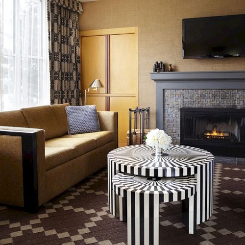 A cozy living room with a sofa, striped ottoman coffee table, TV, fireplace, and blue chairs.