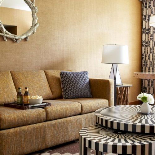 A cozy living room with a patterned sofa, zebra-style tables, lamps, and a window with greenery outside.