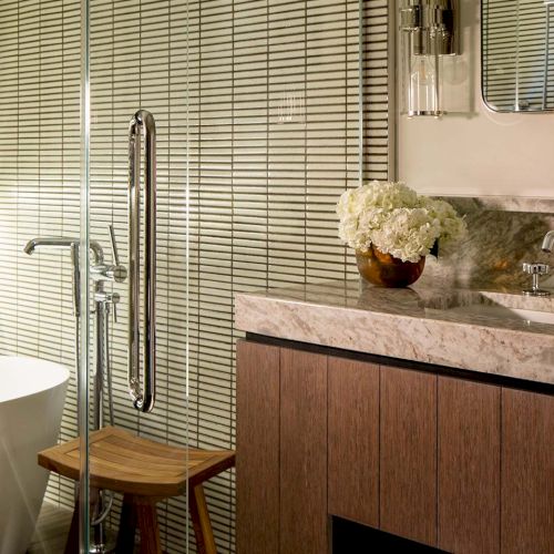 A modern bathroom with a white tub, marble vanity and sink, chrome faucets, and a small vase of white flowers.
