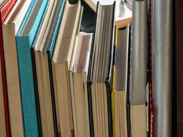 Colorful hardback books packed tightly on a shelf, showing varied spine colors and textures.