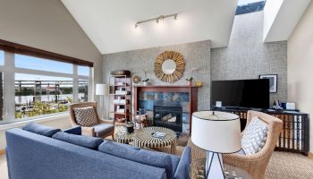 Bright living room with fireplace, TV, sofas, chairs, and large windows overlooking a river.