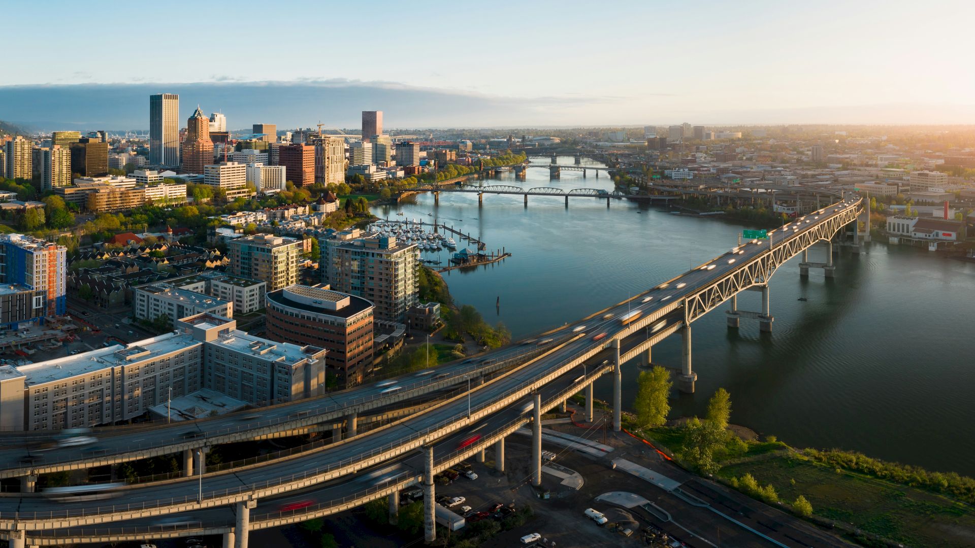 An aerial view of a modern city skyline with a wide river, bustling bridges, and golden-hour sunlight over downtown.
