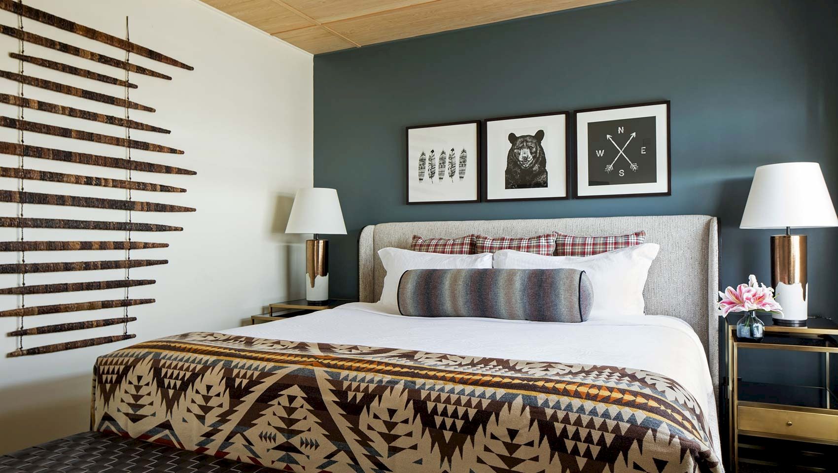 A modern bedroom with a patterned blanket, framed animal wall art, two lamps, and blinds on the window.