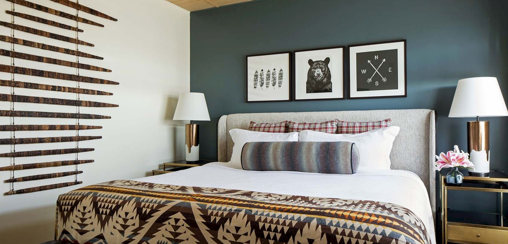 A modern bedroom with a patterned blanket, framed animal wall art, two lamps, and blinds on the window.