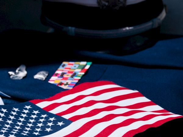 An American flag on a desk with a pair of sunglasses, a colorful card, and small items beside the case.