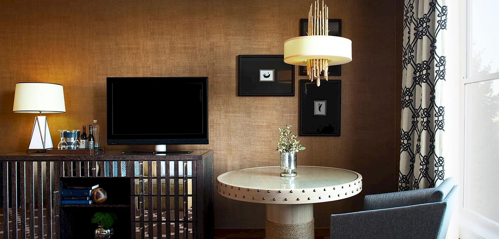 A modern living room with two lamps, a TV on the wall, a round coffee table with flowers, and dark curtains.