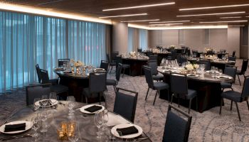 An elegant banquet hall with round tables set for dinner&mdash;plates, glasses, candles, and chairs neatly arranged.