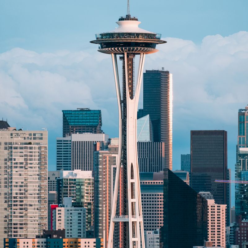 The Space Needle rises above a city skyline, with its saucer-shaped observation deck against a blue sky.