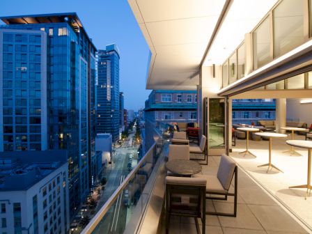 A modern rooftop terrace with seating overlooks downtown skyscrapers at dusk, with streets and buildings stretching into the distance.