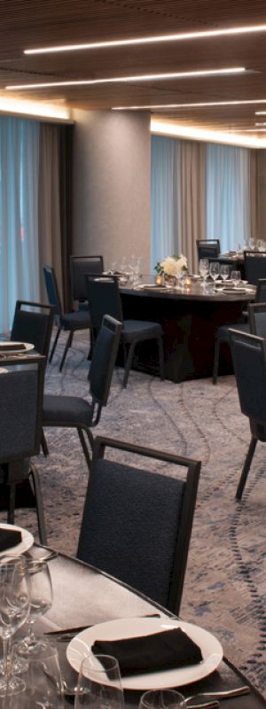 Elegant banquet hall with set dinner tables&mdash;plates, glasses, candles, flowers, and neatly arranged dark chairs.