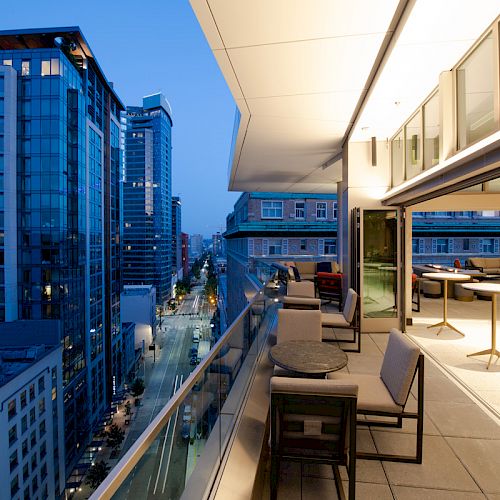 Rooftop terrace with seating overlooks a downtown skyline of tall glass buildings at dusk.