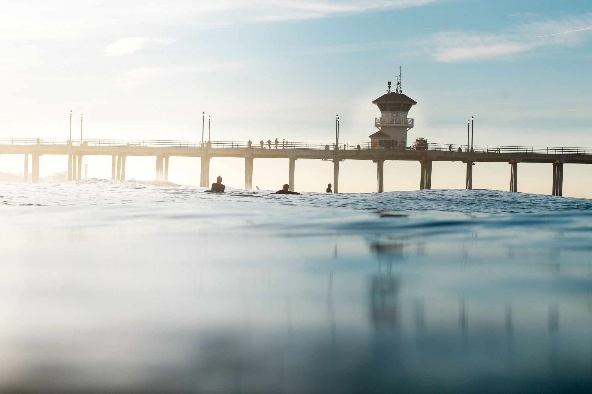 A seaside pier with a lifeguard lookout and people swimming in the waves at calm sunrise.